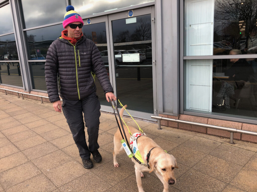 John walks on a pavement with his guide dog daisy. 