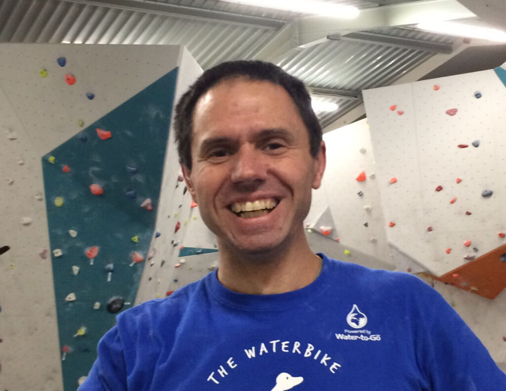 John smiles. Climbing wall panels can be seen in the background