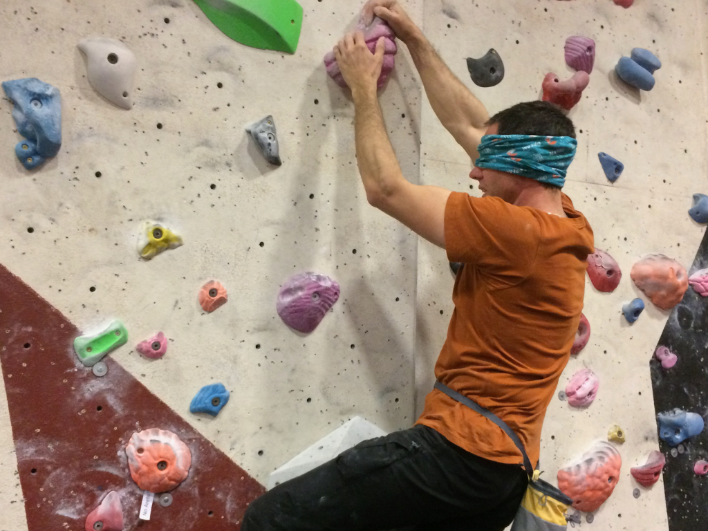 John holds on to a large climbing hold while wearing a blindfold