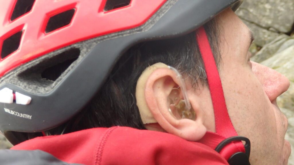 John wears a red helmet. His hearing aids are visable