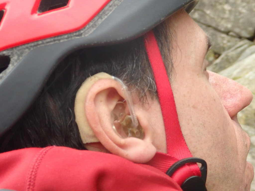 John wears a red helmet. His hearing aids are visible