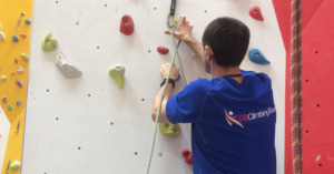 A climber is low down on a climbing wall clipping the rope into a quickdraw